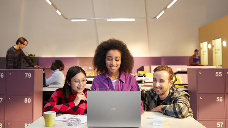 Three people in the office are looking at a gram together with smiling.
