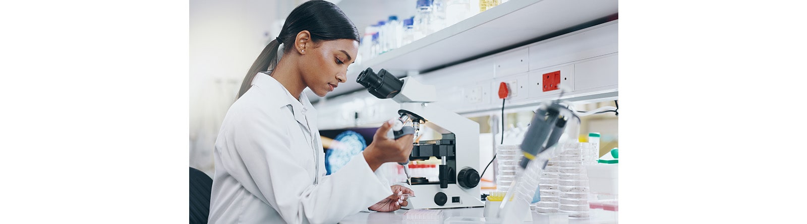 A scientist in a lab coat works in a laboratory, examining a sample with a pipette near a microscope.