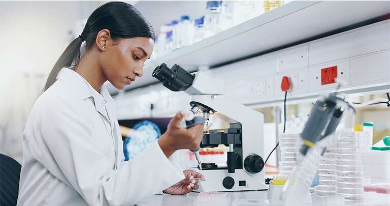 A scientist in a lab coat works in a laboratory, examining a sample with a pipette near a microscope.