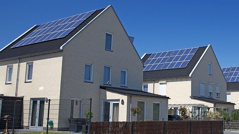 The front-side view of ivory-tone houses is displayed side by side with the black roof covered with solar panels. 