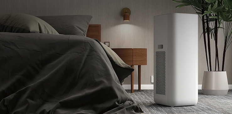 Cozy bedroom with an LG dehumidifier placed beside a bed, showcasing sleek design and moisture control functionality in a comfortable residential environment.