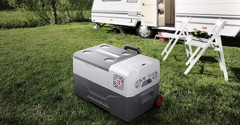 A sleek portable refrigerator in a shade of gray sits prominently beside a camper van, ready for outdoor activities.