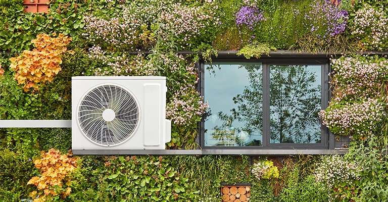 An outdoor ac unit beside the window with grass and colorful flowers as background