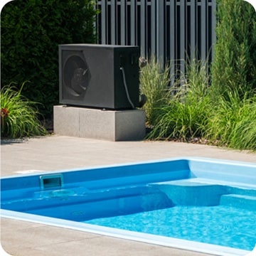 Green plants surround an outdoor pool with a black heat pump on a concrete platform.