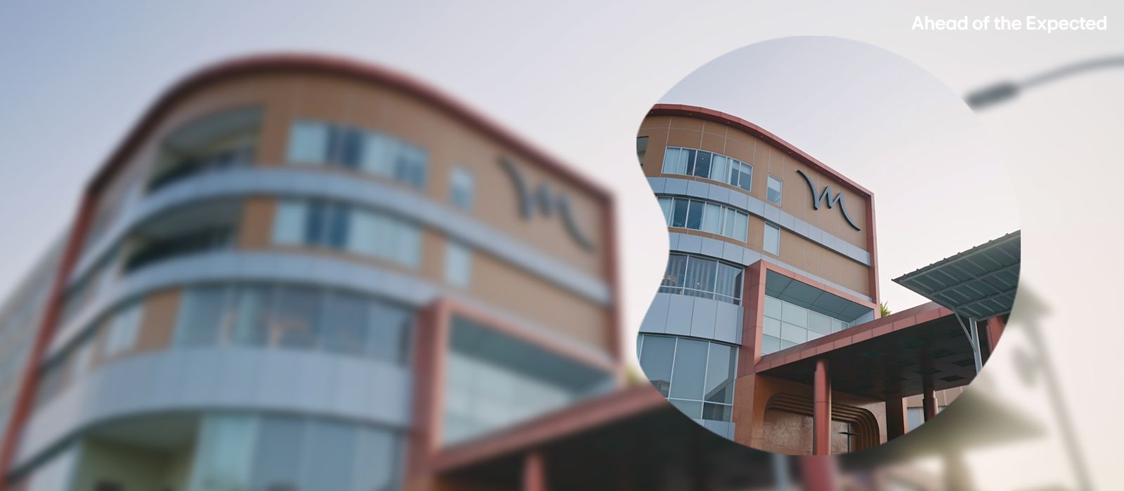 Modern building with curved facade and red accents, featuring a stylized M logo and the phrase 'Ahead of the Expected