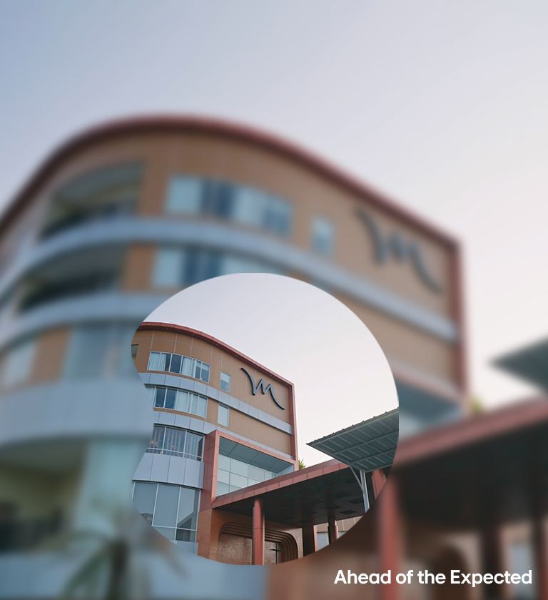 Modern building with curved facade and red accents, featuring a stylized M logo and the phrase 'Ahead of the Expected