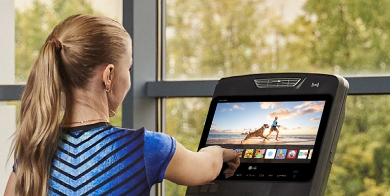 A woman is touching an icon on a TV screen installed on an exercise machine.
