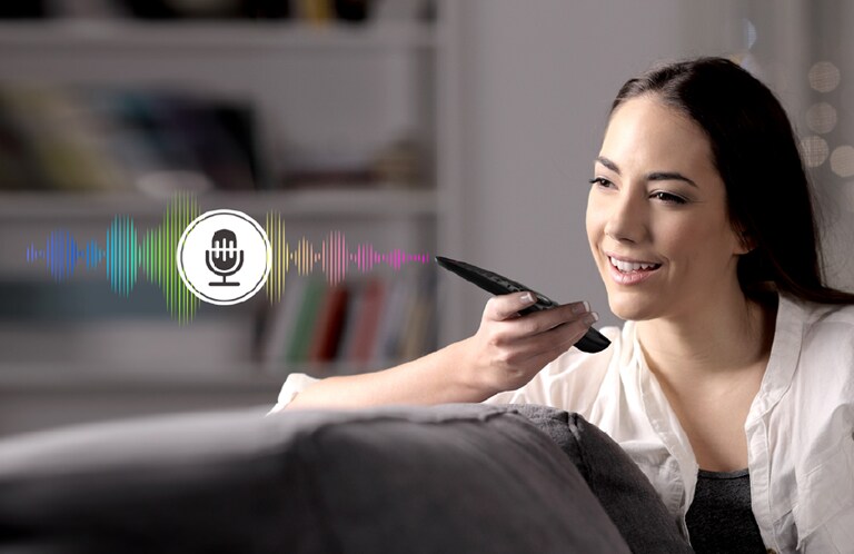 A woman is controlling TV by speaking to a remote control which has voice recognition.