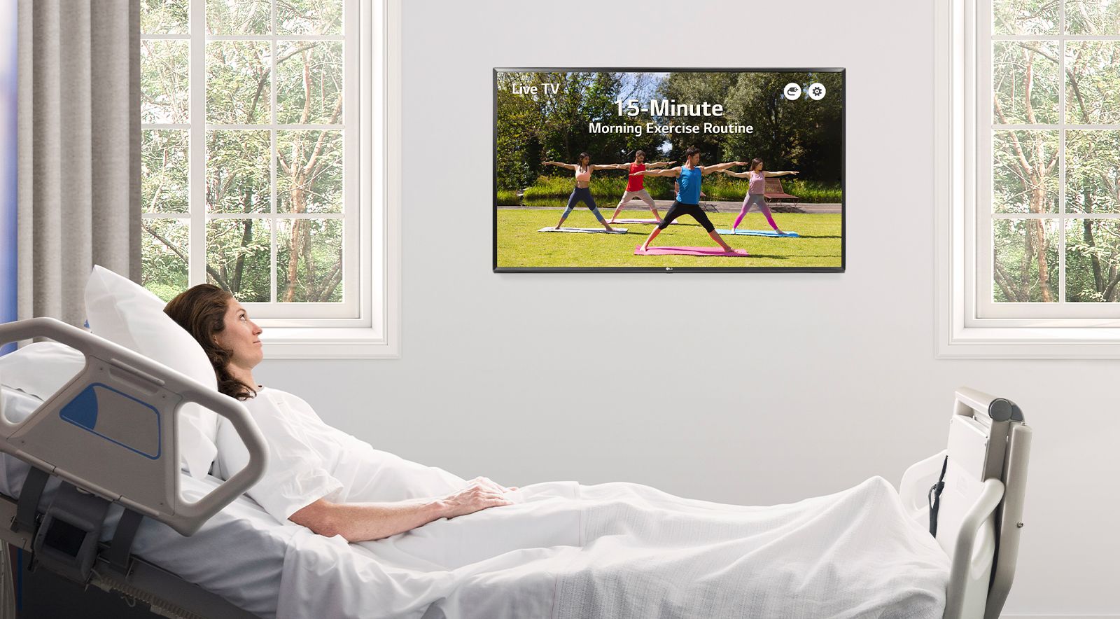 The patient is lying in the hospital room’s bed and watching the TV hanging on the wall.