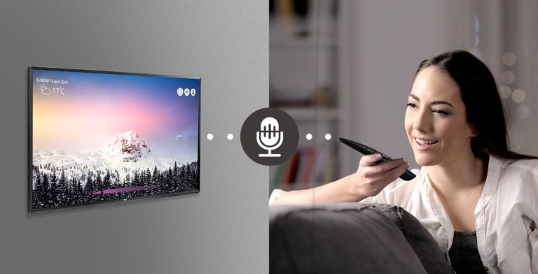 A woman is controlling TV by speaking to a remote control which has voice recognition.