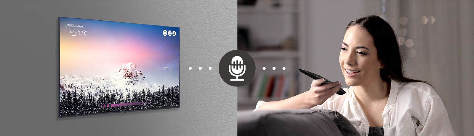 A woman is controlling TV by speaking to a remote control which has voice recognition.