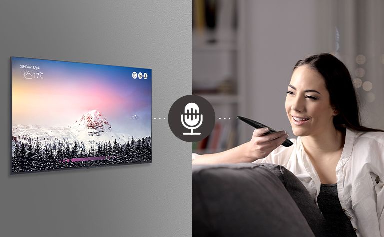 A woman is controlling TV by speaking to a remote control which has voice recognition.