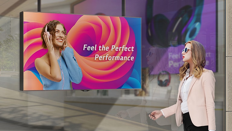 A woman wearing sunglasses is watching ads on the display installed in a shop window, and the ads on the display are very visible even under the strong sunlight.