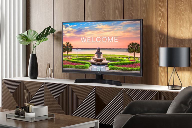 A TV is placed on the hotel room's main shelf, and a welcome message for guests is displayed on the screen.