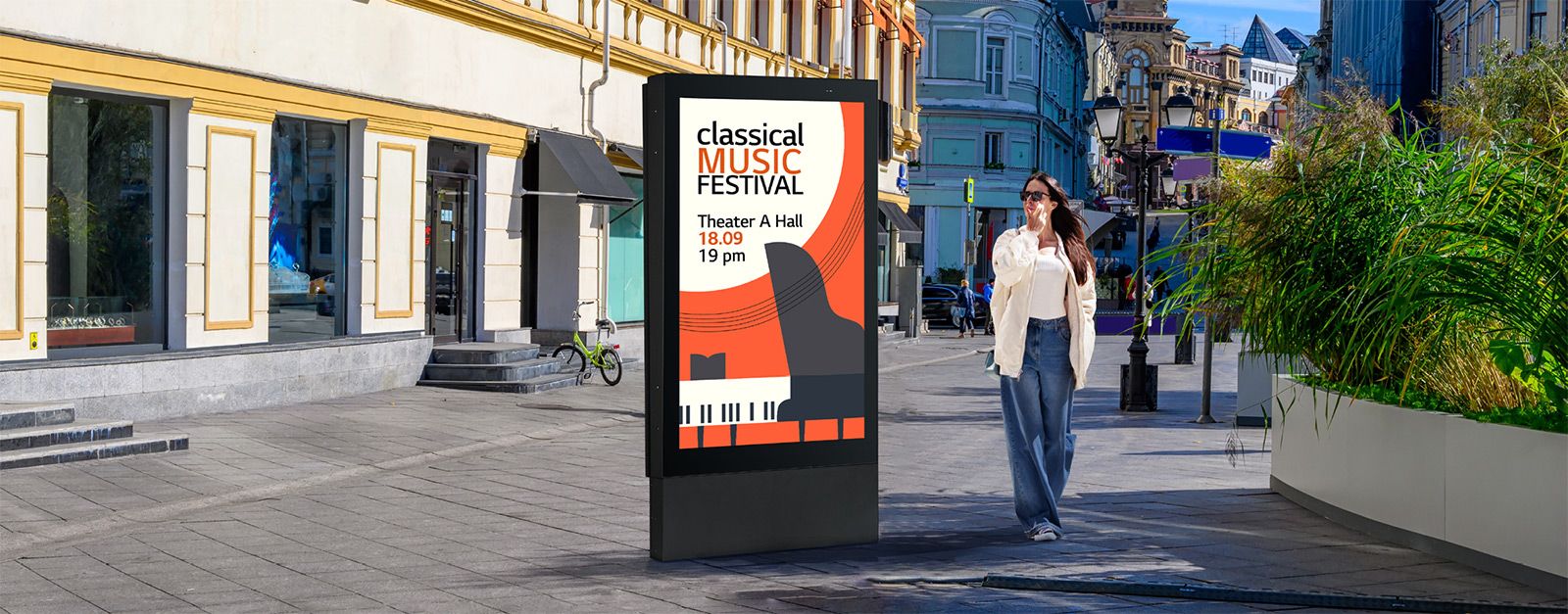 A large-sized display is installed on the street, and a woman is looking at a vivid-quality advertisement on the screen.