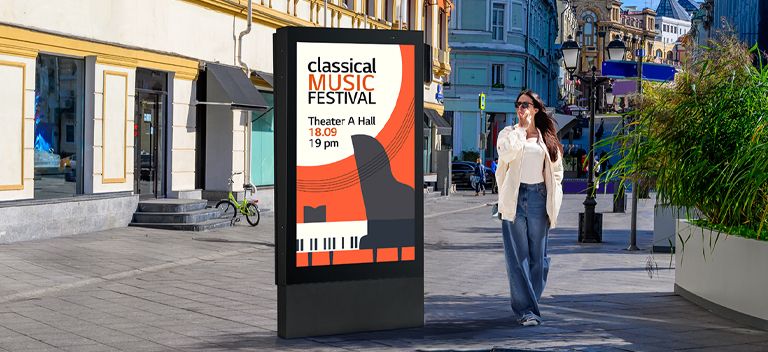 A large-sized display is installed on the street, and a woman is looking at a vivid-quality advertisement on the screen.