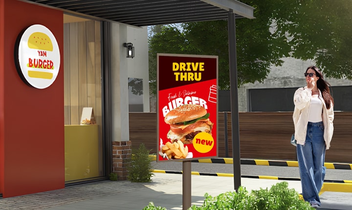 An XE4P is installed outside a burger shop, and a woman is looking at a vivid advertisement on the screen.