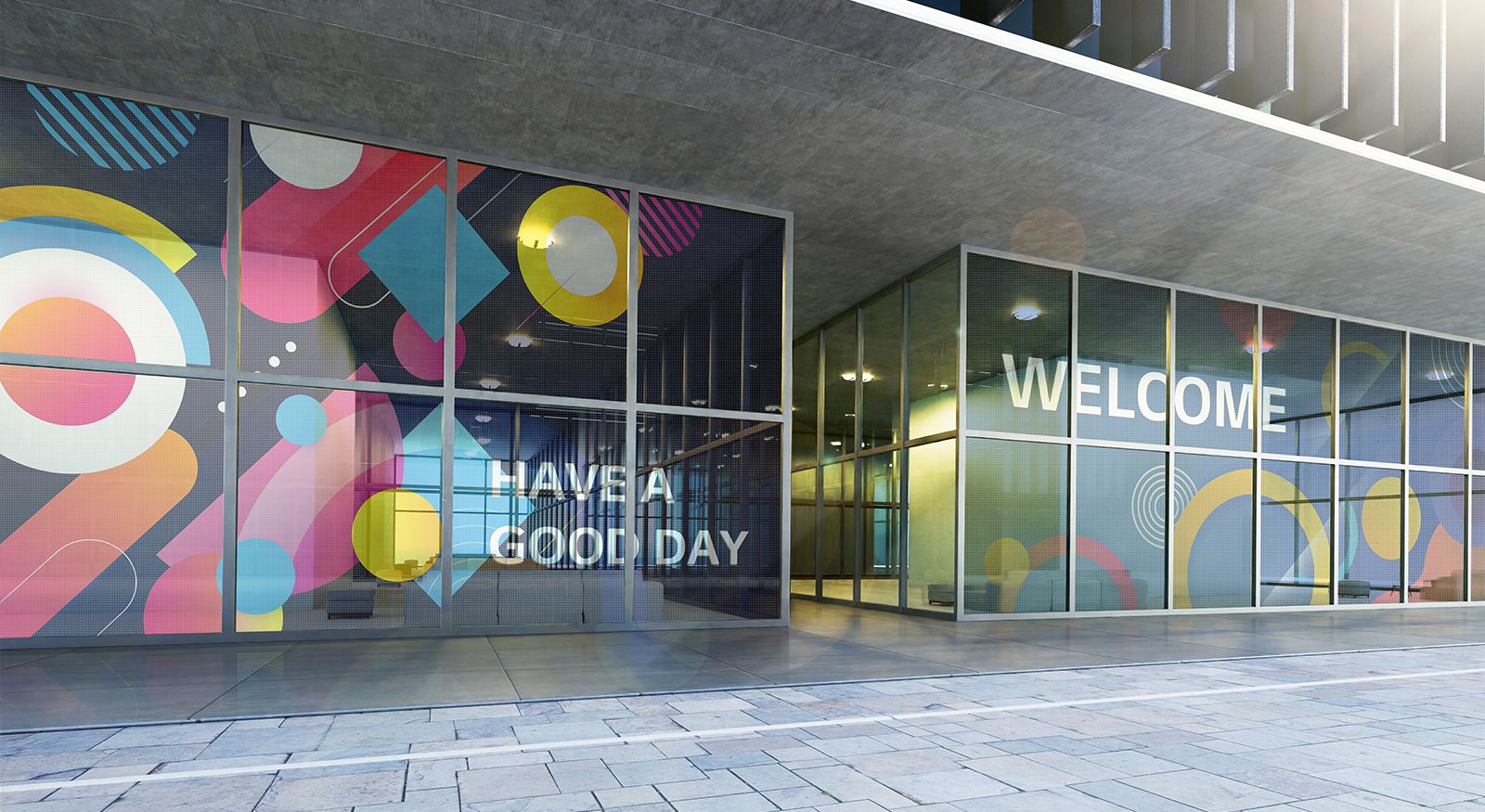 The transparent LED films installed on the glass wall at the building's entrance show content welcoming visitors. Some of the content shows the color well, and some of it looks transparent enough for the background behind the LED films to be seen.
