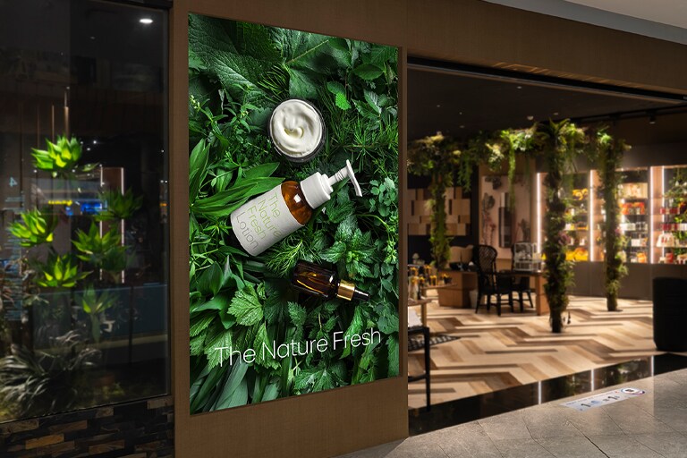 A large LED display is integrated with the wall next to a store entrance in a shopping mall, clearly displaying an advertisement.