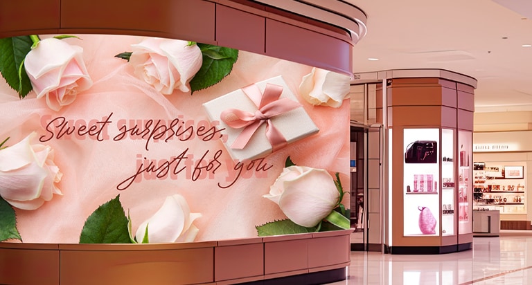 The LSCD is installed along the wide, curved surface of a pillar in a shopping mall, seamlessly displaying advertisements across the curved LED screen.