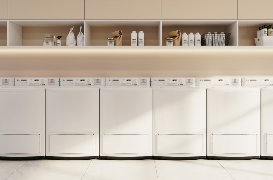 Laundromat with six top-load washers arranged in a row, featuring shelves above them stocked with laundry supplies.