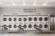 LG Laundry Lounge is shown from the front, featuring installations of the LG Giant Washer, LG Titan, and LG Styler, with desks and chairs arranged in the space.
