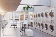 Laundromat features LG Commercial Laundry machines, with single-stack washers on the left and stacked washers on the right. In the center, there is a table for organizing laundry and carts.