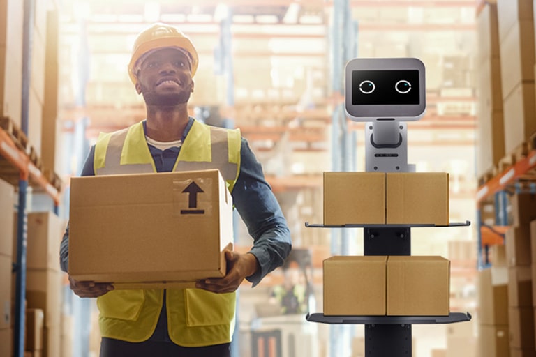 A man and the CarryBot is working side-by-side carrying a box facing the front	