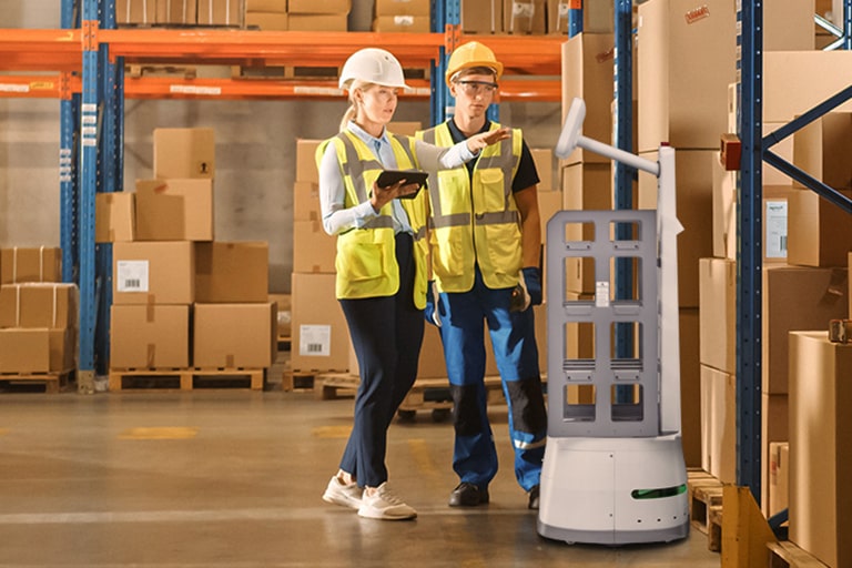 Two workers in a container space one is pointing to the CarryBot facing the workers.	