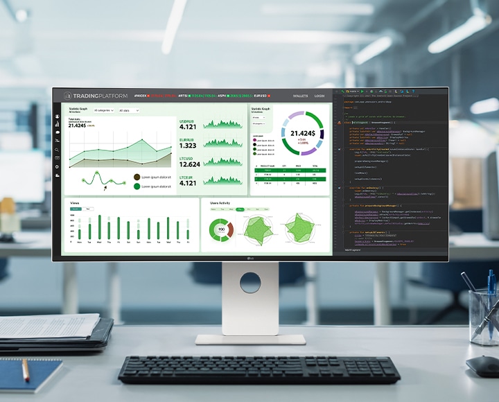 LG UltraFine monitor on an office desk, displaying a trading dashboard and coding interface in a modern workspace.