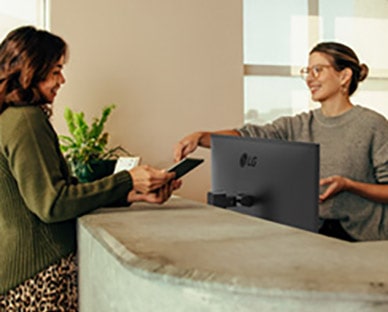 Friendly receptionist showing a woman where to sign on a digital tablet. 
