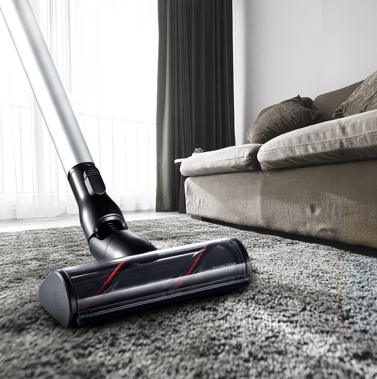 He's pushing a vacuum in the living room.