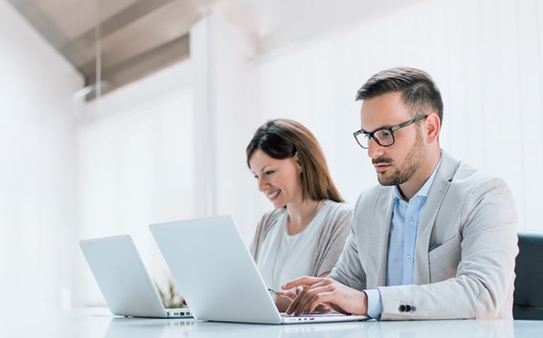 Two administrators are managing devices using LG SuperSign Control+ on personal PCs.