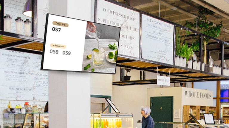 A signage screen mounted on a store wall displays menu images and related information.