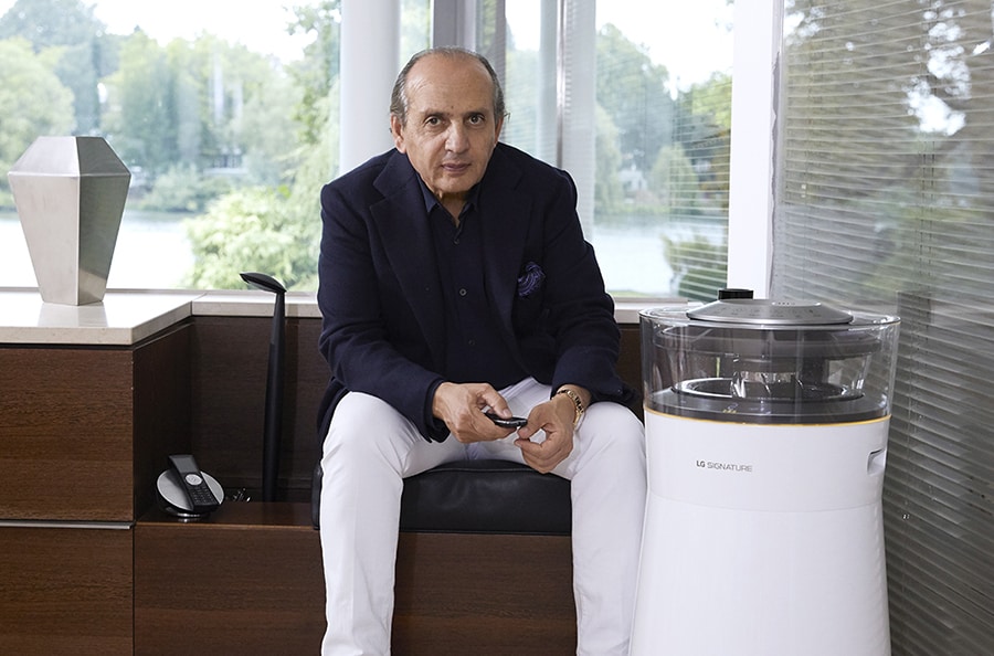 hadi teherani is sitting on a couch and lg signature air purifier is laid right in front of him