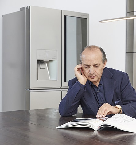 hadi teherani is reading a book while resting his chin on his hand and lg signature refrigerator is laid back of him