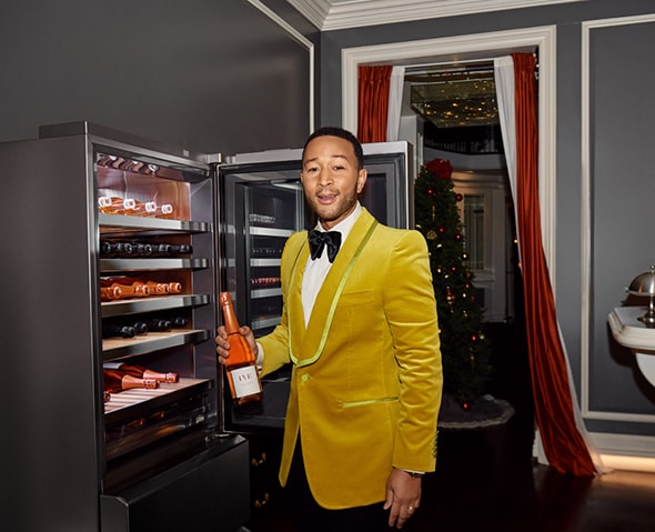 Singer John Legend posing while holding a bottle of wine in front of an LG SIGNATURE Wine Cellar.