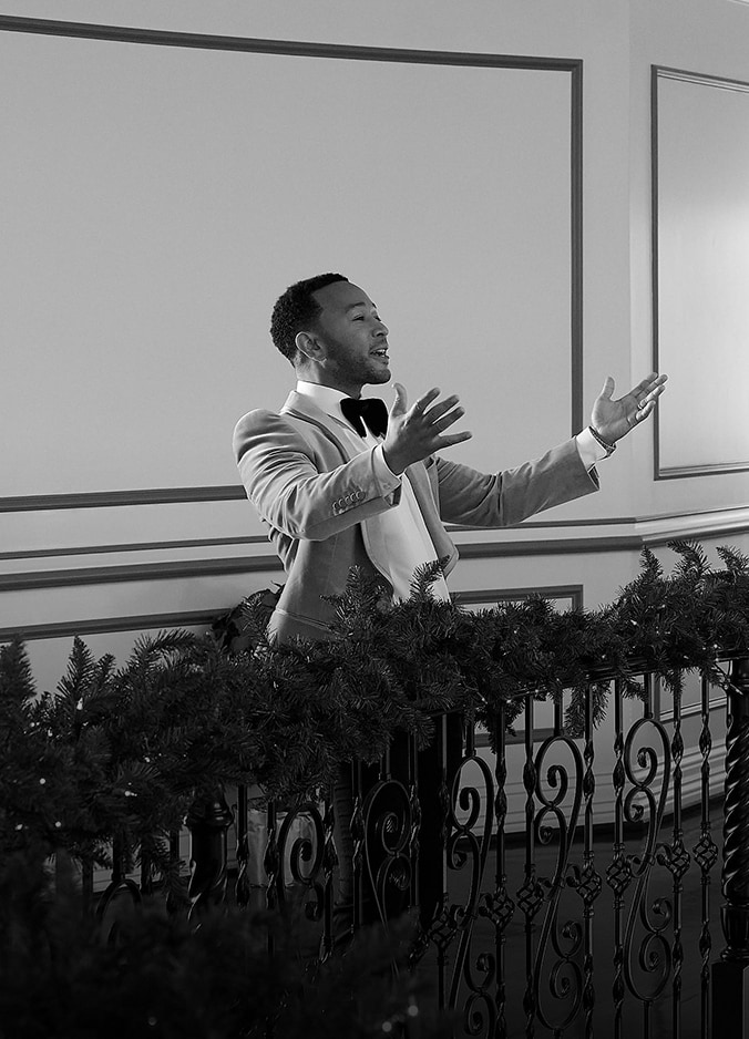 Singer John Legend walking down a staircase holding onto a handrail decorated with Christmas decoration.