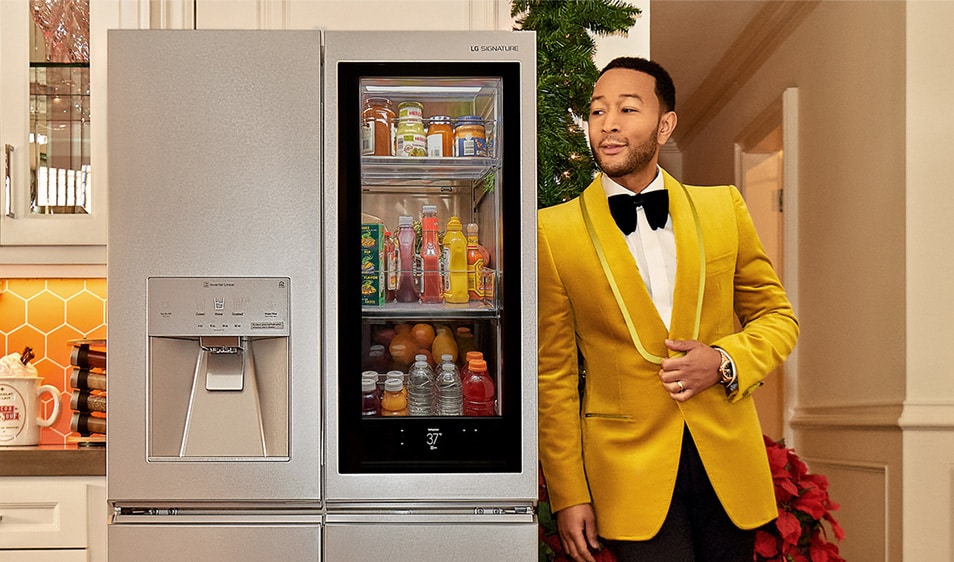 John Legend leaning slightly on a refrigerator with a see-through door