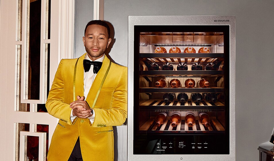 John Legend clasping his hands next to an electronic wine cellar holding 15 bottles of wine