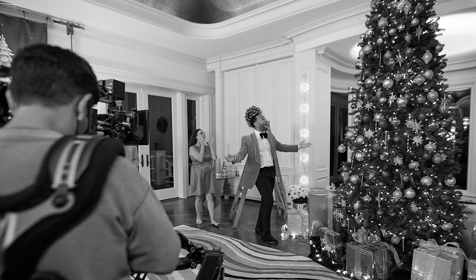 John Legend being filmed next to a tall Christmas tree with ornaments