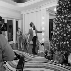 John Legend being filmed next to a tall Christmas tree with ornaments