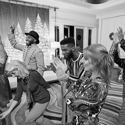 Six people clapping and laughing in a room decorated for Christmas