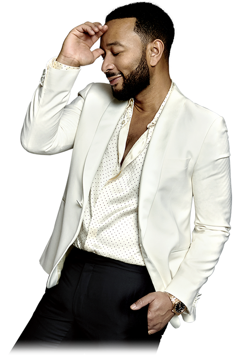 John Legend in a white shirt and jacket, smiling with one hand at his forehead and one in his pocket