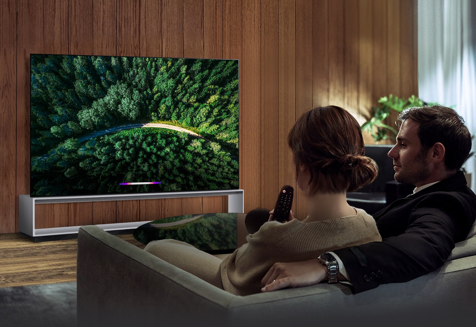 Two people are sitting on the couch and watching tv that is LG SIGNATURE OLED TV Z9