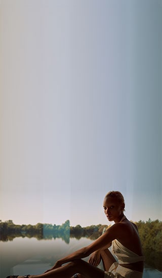 Image of a model wearing one of the Winter Sun capsule collection pieces sitting  in front of a beautiful lake