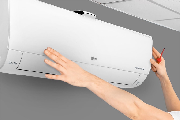 Side view of an air conditioner on the wall.  Two hands reach for the air conditioner, one holding a tool, suggesting ease of installation.