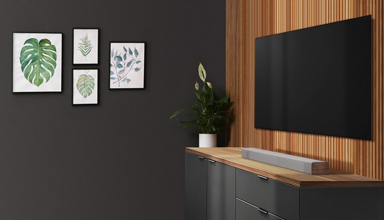 Ένα soundbar και μια τηλεόραση τοποθετημένα σε έναν τοίχο με ξύλινη επένδυση. Στον σκούρο τοίχο είναι αναρτημένα τέσσερα κάδρα με εικόνες.