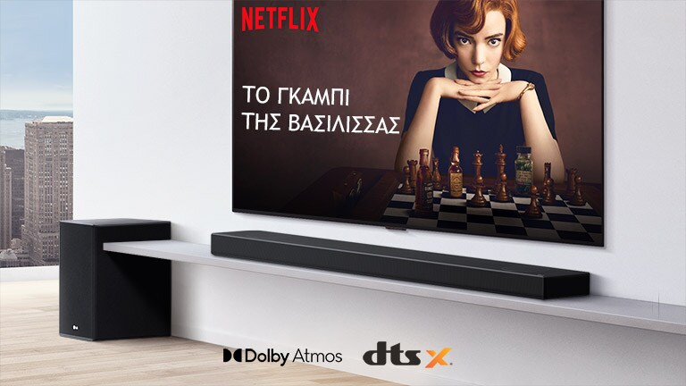 Η τηλεόραση είναι τοποθετημένη στον τοίχο. Στην οθόνη της τηλεόρασης φαίνεται η αφίσα μιας τηλεοπτικής σειράς. Το LG Soundbar βρίσκεται ακριβώς κάτω από την τηλεόραση σε ένα λευκό ράφι, με ένα subwoofer ακριβώς δίπλα. Στο κάτω ενδιάμεσο μέρος της εικόνας φαίνονται τα λογότυπα Dolby Atmos και DTS:X.