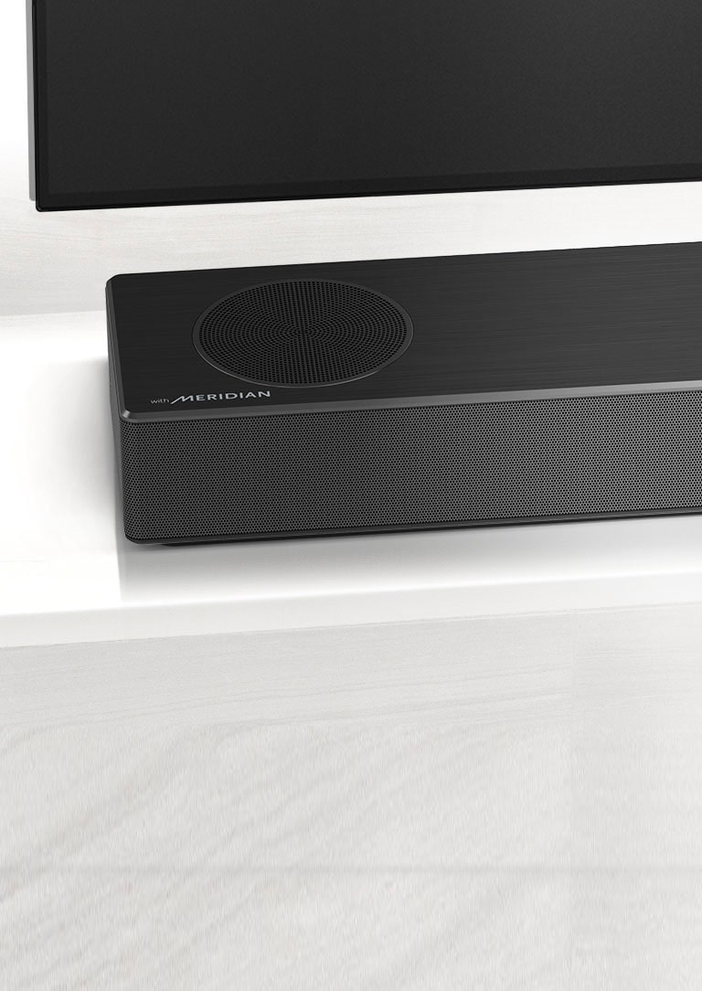 Κοντινό του LG Sound Bar με το λογότυπο της Meridian κάτω αριστερά. Φαίνεται και η κάτω αριστερή πλευρά της τηλεόρασης.
